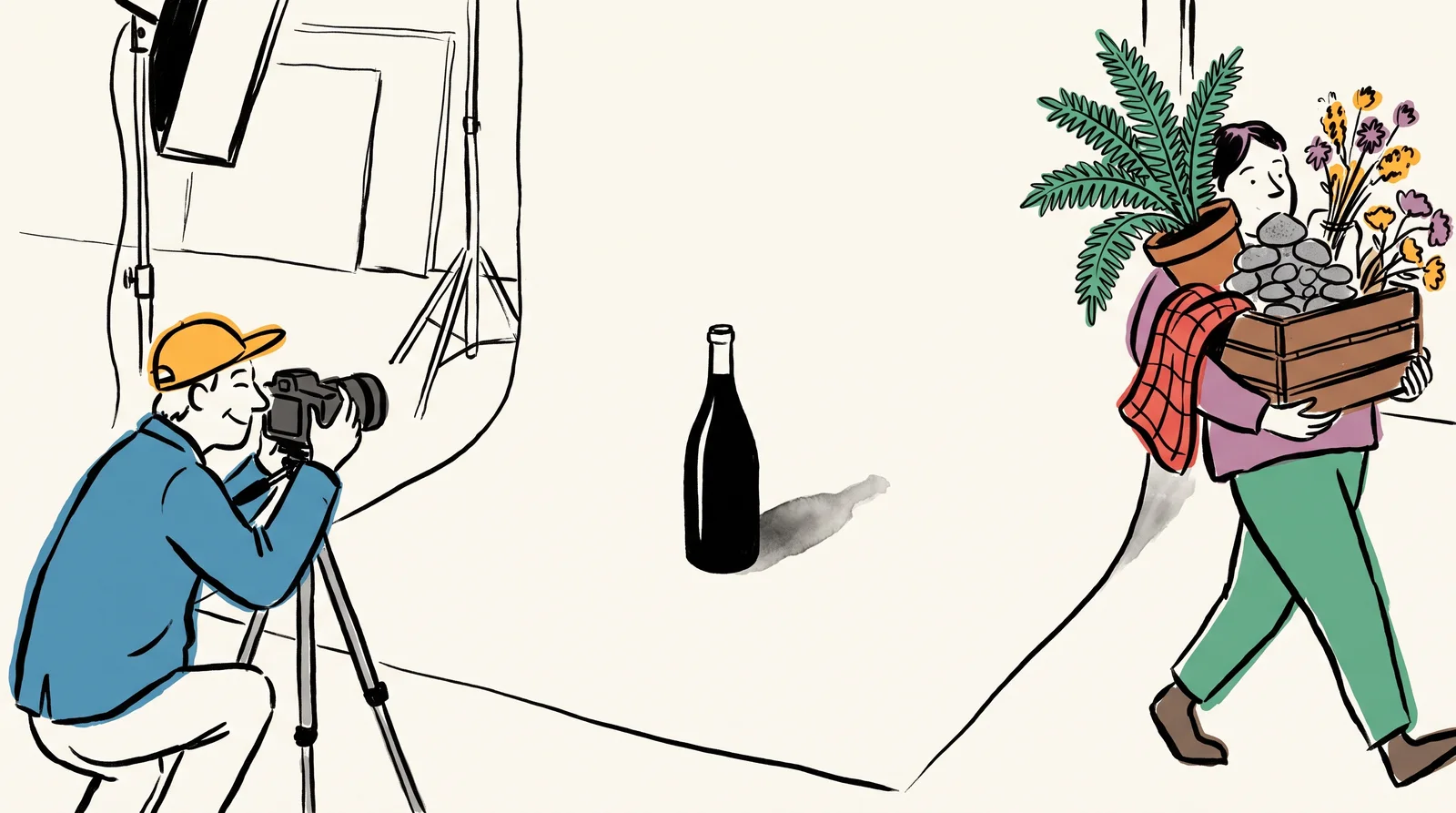 A photographer behind a camera looks at a single bottle on white paper while an assistant carries away a fern, cloth, pebbles and a crate.